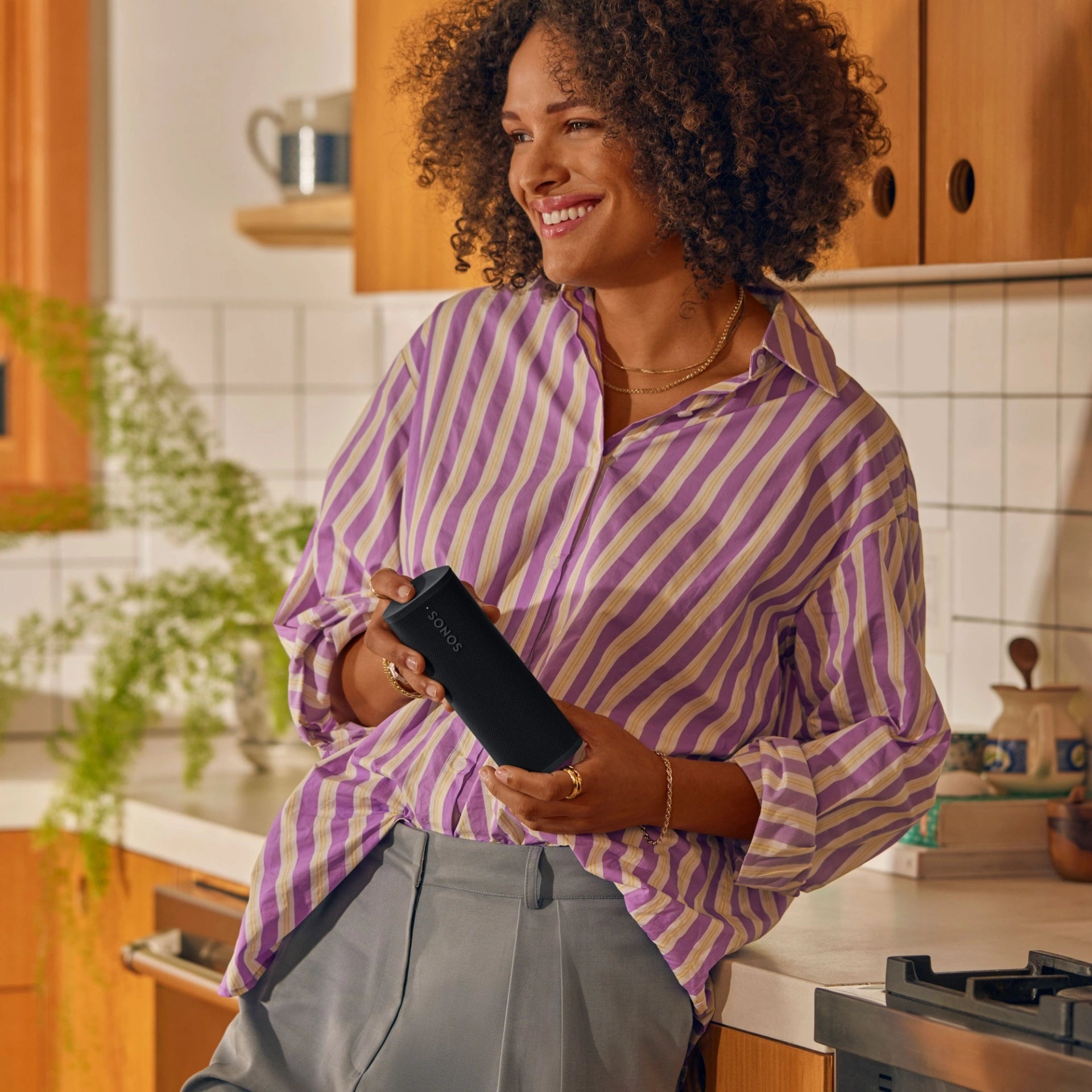 Lifestyle image of a female in a kitchen holding a Sonos Roam 2 Portable Speaker Black in her hands.